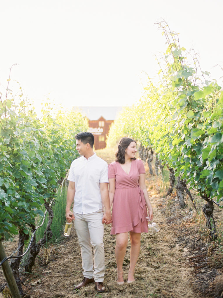 an engaged couple hold hands in the Hillside winery vineyard 