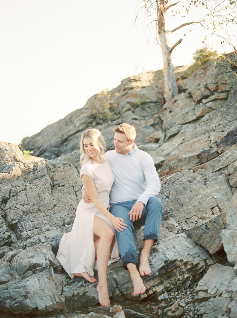 an engaged couple sitting on rocks at Kelowna beach 