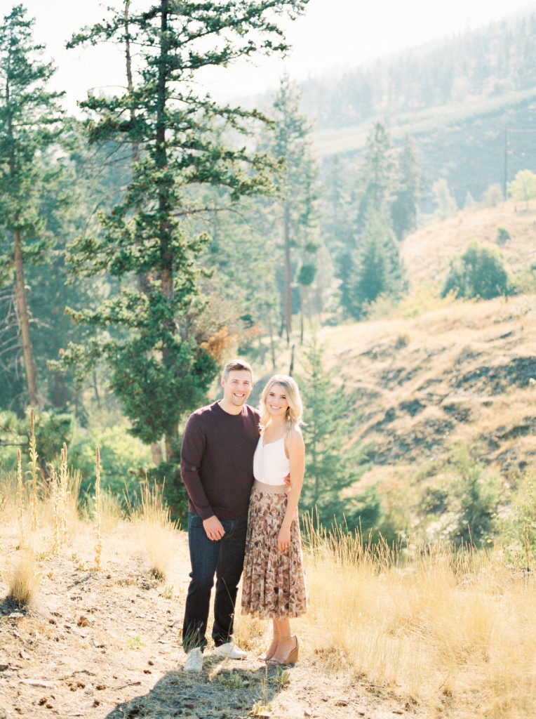a couple smile for engagement photos on a cliff in Kelowna 