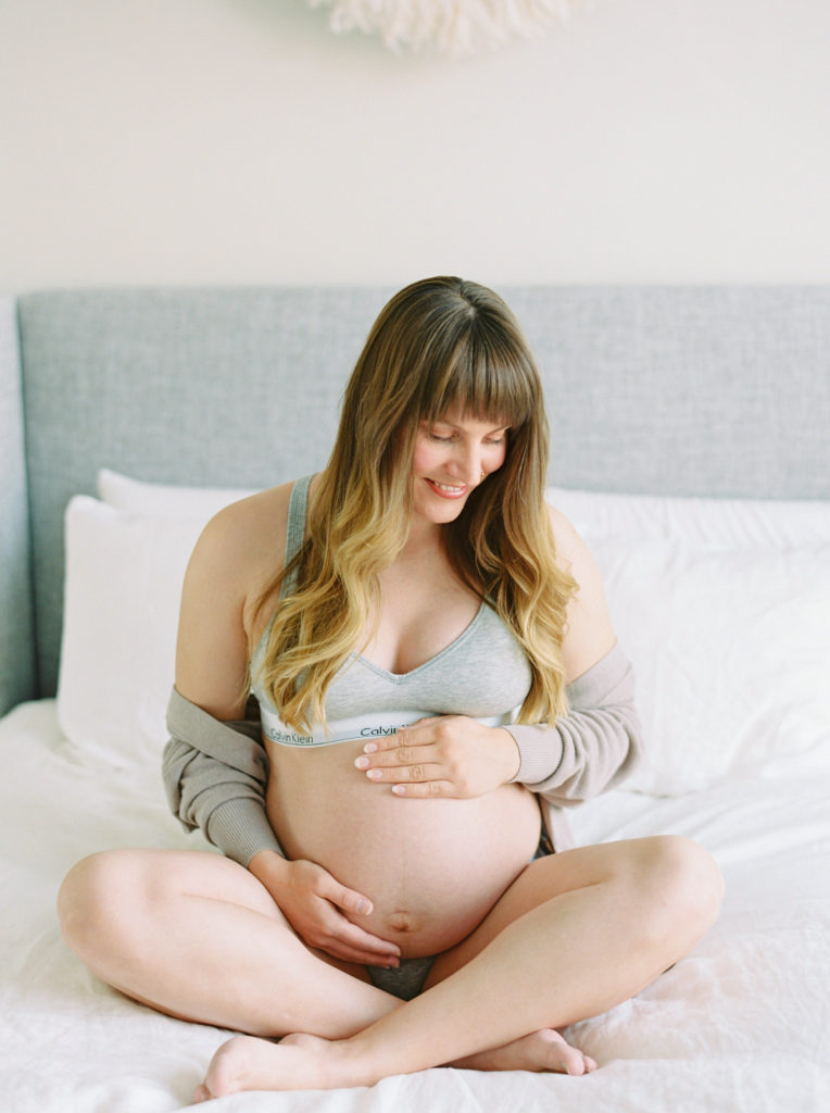 mom to be holding her pregnant belly for her at home maternity photos 