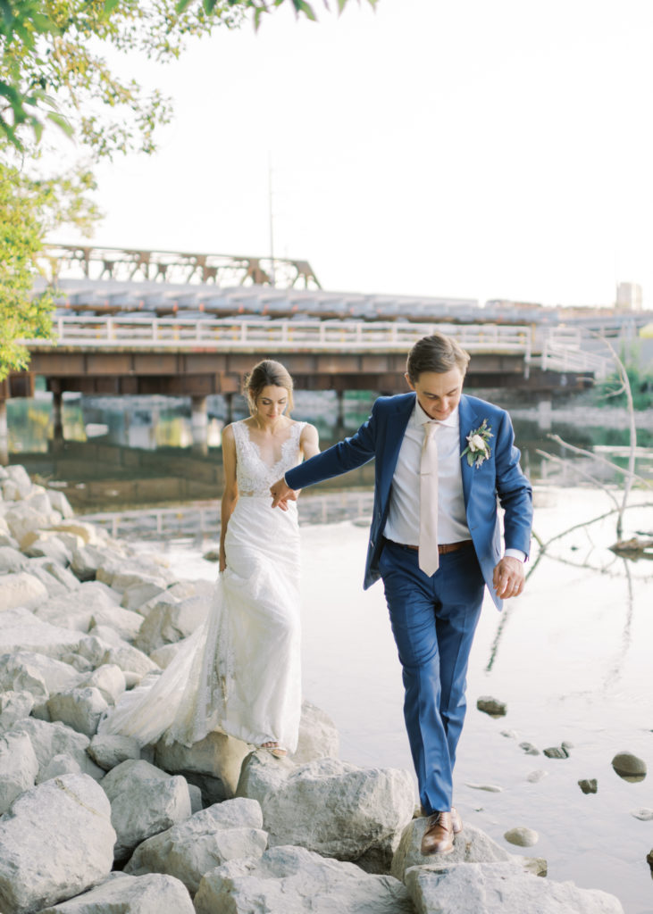 a groom leads his bride across a rocky beach 