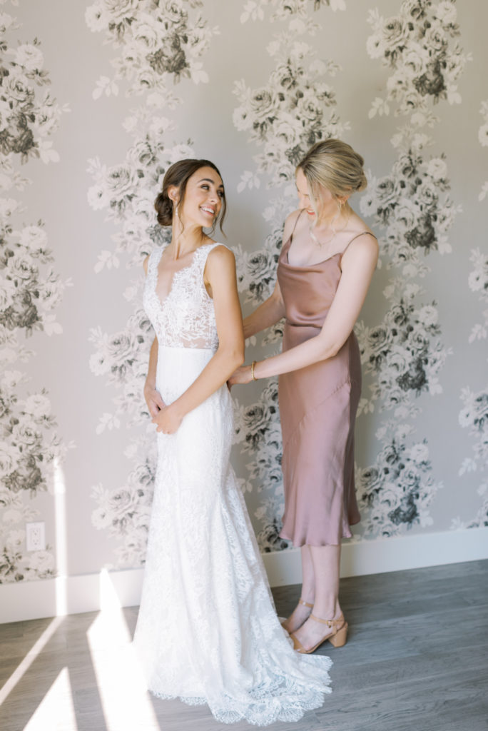 a brides sister helping her into her wedding dress 
