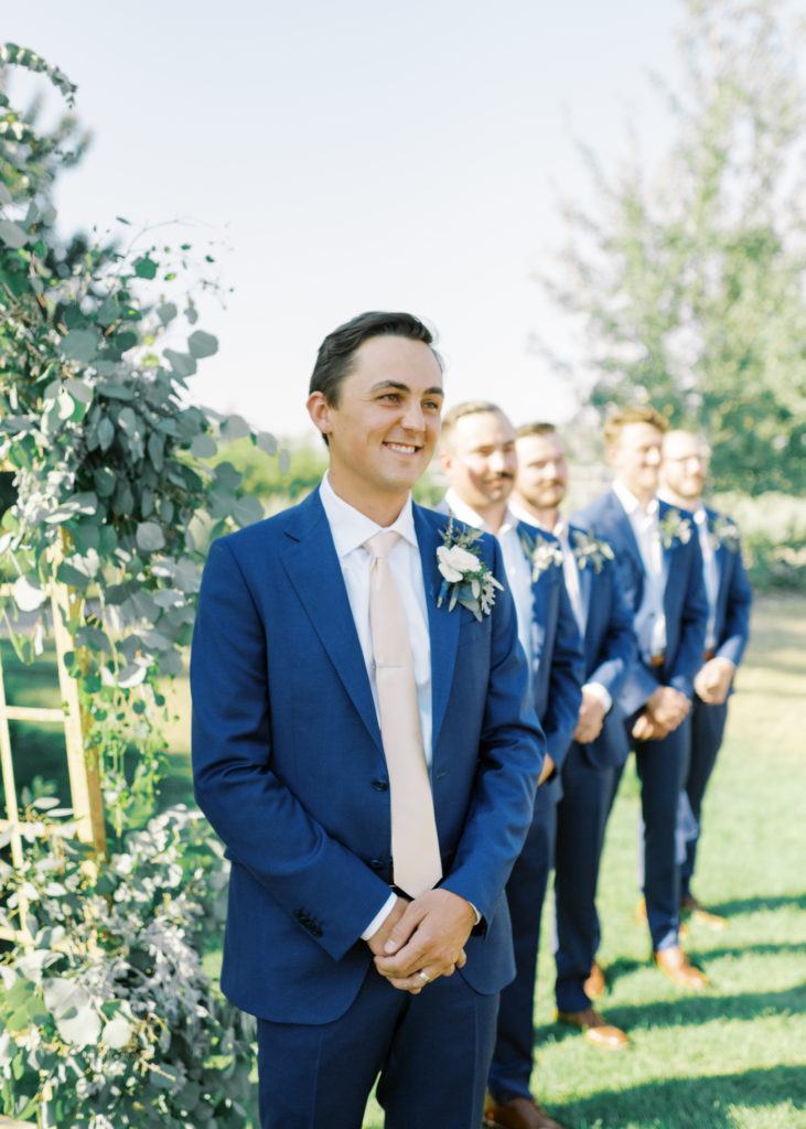 a smiling groom watches his bride walk down the aisle 