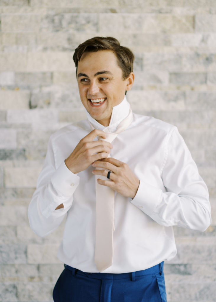 a groom tying his champagne tie 