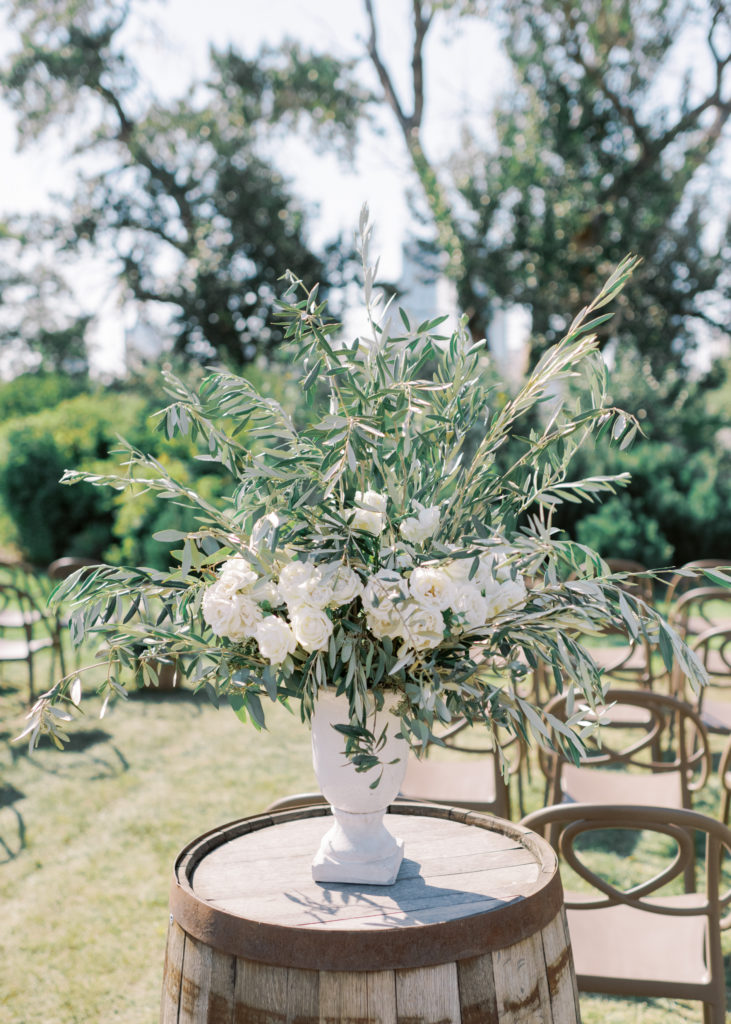 an elegant white wedding ceremony floral arrangement on a wine barrel 