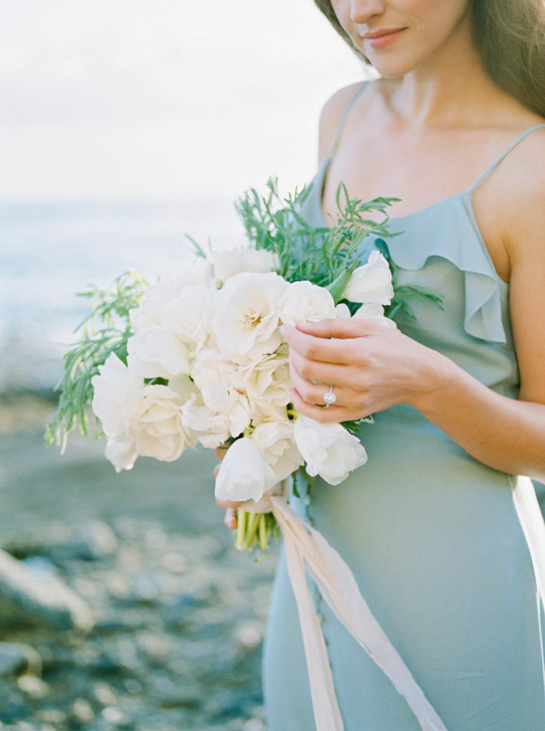 a woman wearing an engagement ring holding a white bouquet