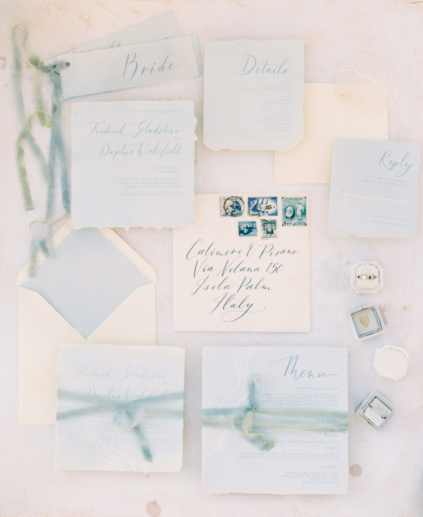 blue and cream wedding stationary arranged for a photo with wedding rings