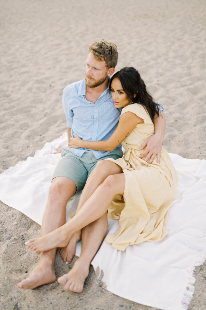 a couple pose on blanket for their Kelowna beach engagement session 