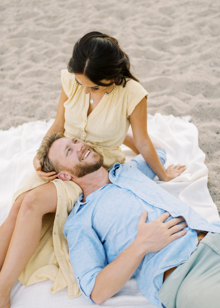 a man laughs with his fiancé on the beach 