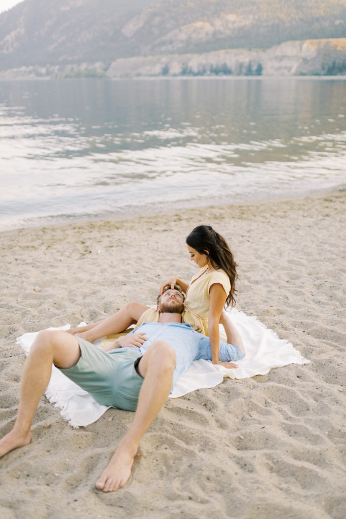 an engaged couple relaxing on the beach for their Kelowna beach engagement session