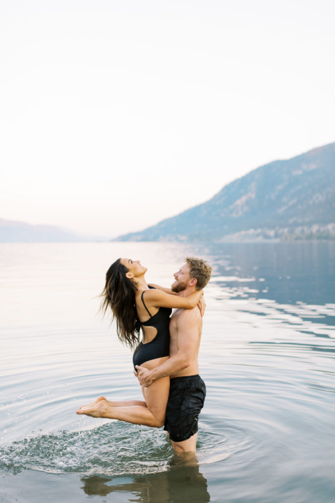 a man and woman play in Okanagan lake at their Kelowna beach engagement session 
