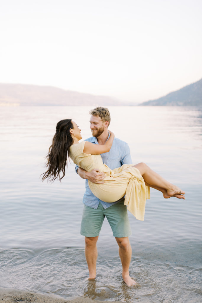 a man lifts his fiancé for their Kelowna beach engagement session 