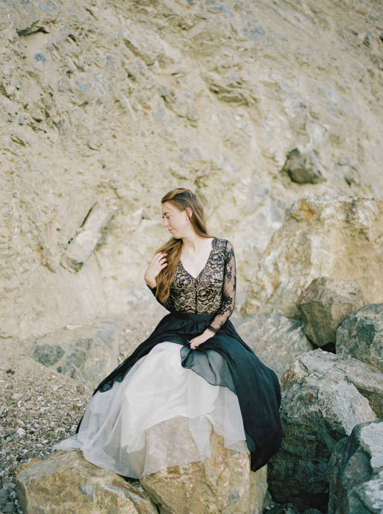 a bride in a black wedding dress poses on a rock 