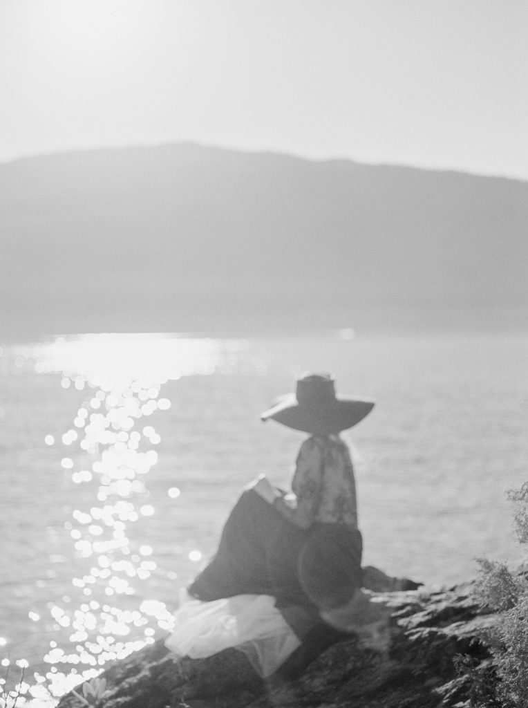 a bride in black sits on a rock by the Okanagan lake 