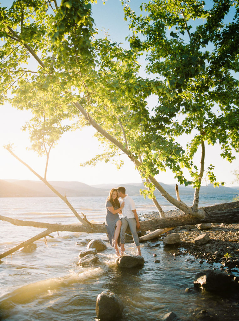 an engaged couple sit on a tree over Okanagan Lake 
