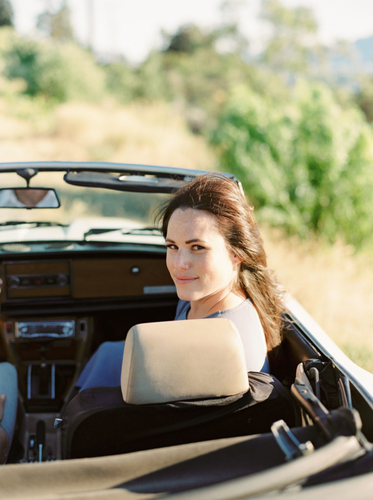 a woman smiles in a convertible car 