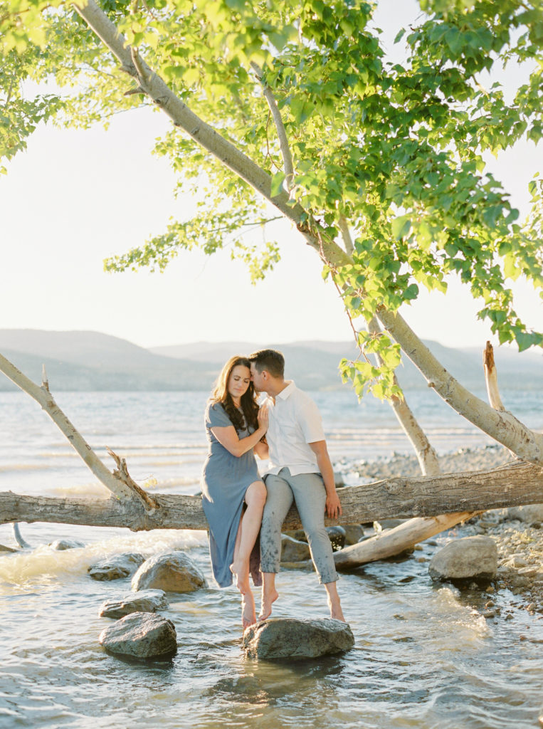 a couple pose on a tree over a lake for their Okanagan couples session 